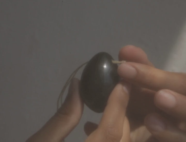 hands holding and stringing a jade yoni egg